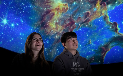A male and female student inside the new planetarium with a 30-foot dome viewing the galaxy.