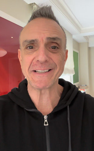 Hank Azaria, in a classic black zip-up, delivers a personal video invite to join him and his Bruce Springsteen tribute band for a night of unforgettable music and fun.
