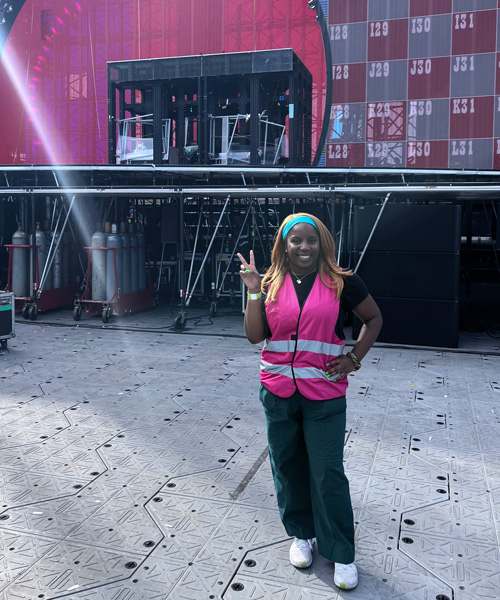 Miami Golde in a pink work vest giving the peace sign in front of a stage prior to the Beyoncé concert