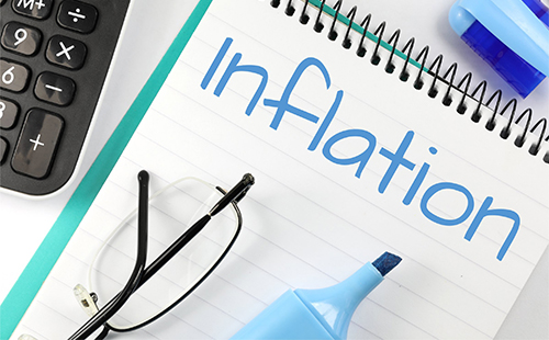 Inflation written on note pad next to calculator, glasses, and a highlighter.