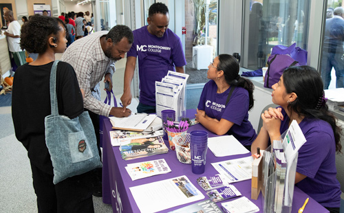 Students around a table with flyers talking with Community Engagement staff who are seated or standing